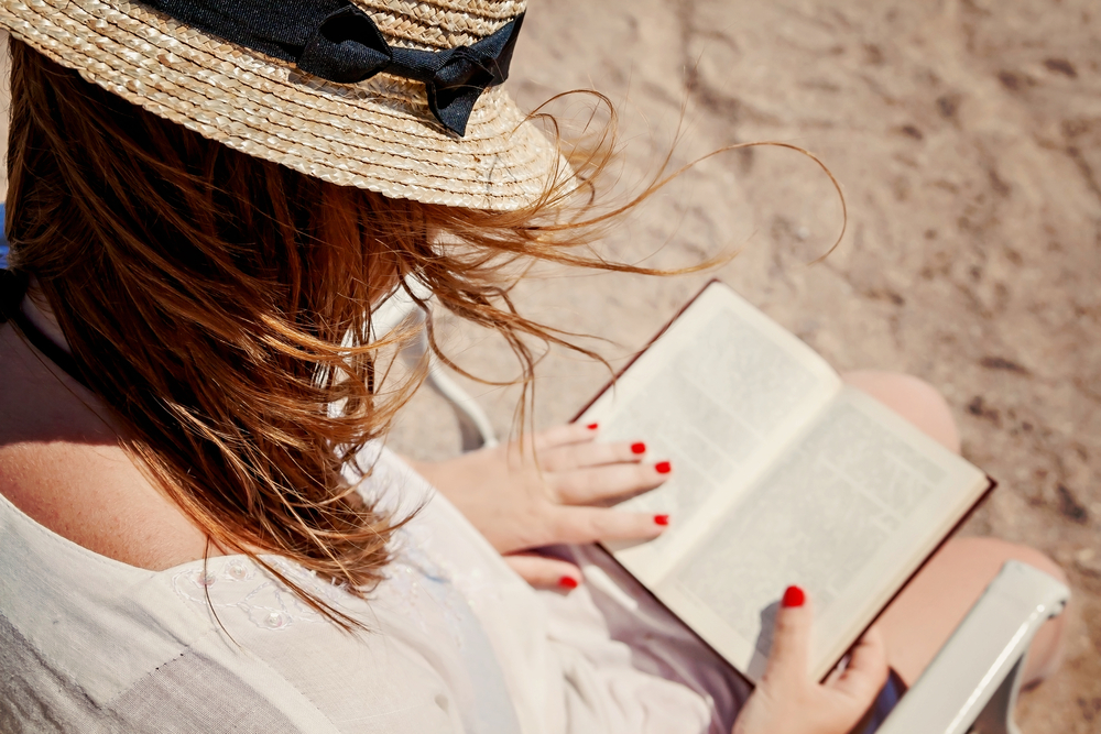 Buch lesen am Strand, im Sommer, Frau mit Strohhut hält ihr geliebtes Buch in der Hand